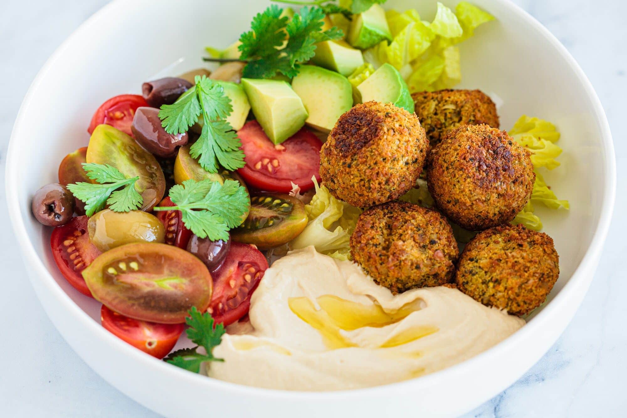 Falafel plate with salad, tomatoes, avocado, hummus and olives.