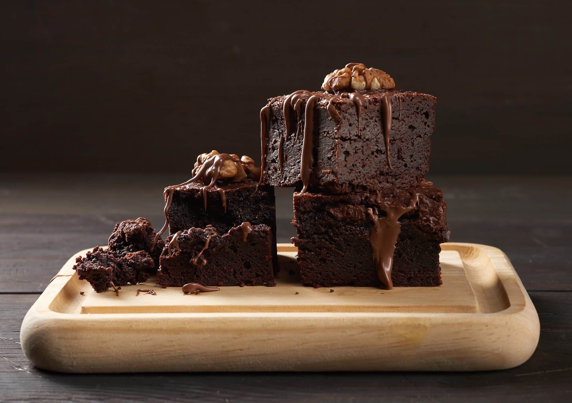 Stack of baked square pieces of chocolate brownie cake on brown wooden cutting board