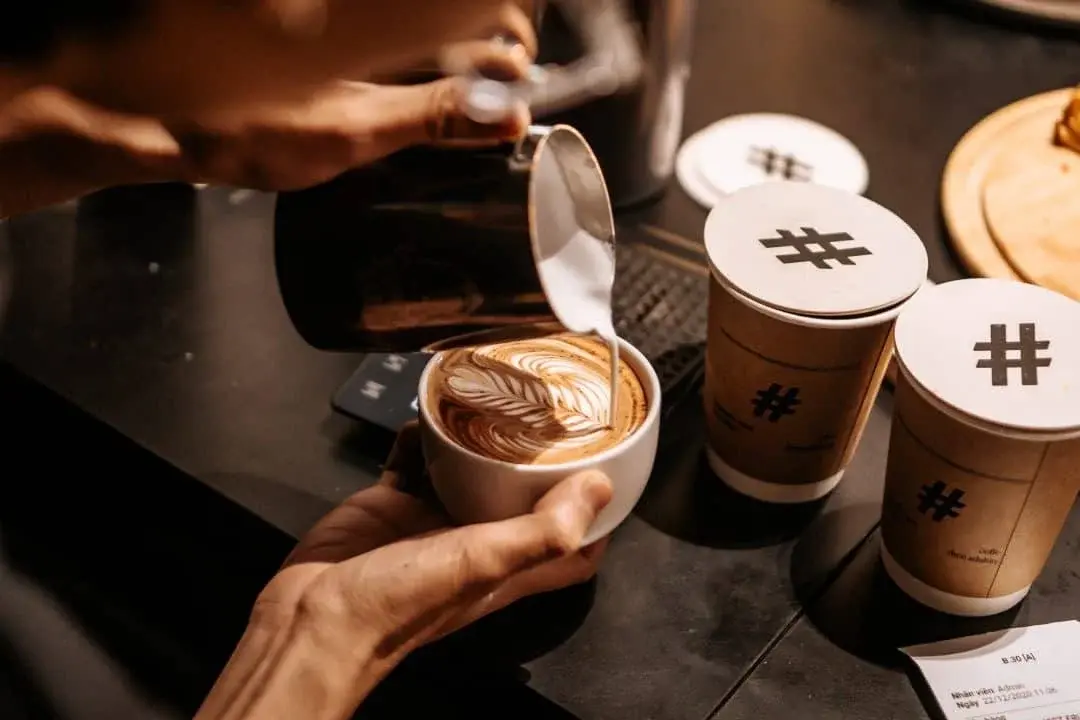 Professional barista pouring latte art coffee at Pearl Lemon Catering event in Barcelona with branded takeaway cups