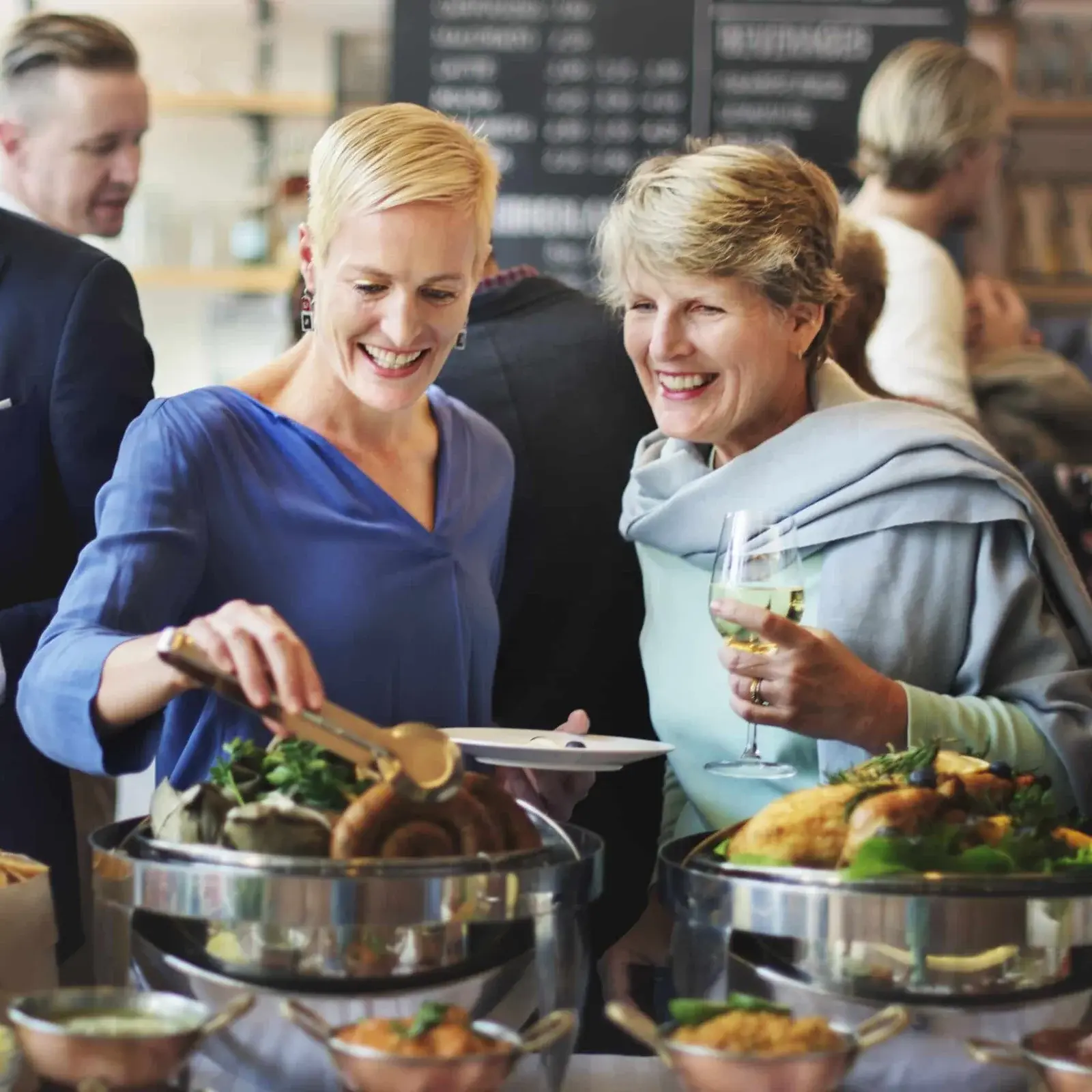Two women enjoying buffet-style corporate catering event with hot food stations by Pearl Lemon Catering Barcelona