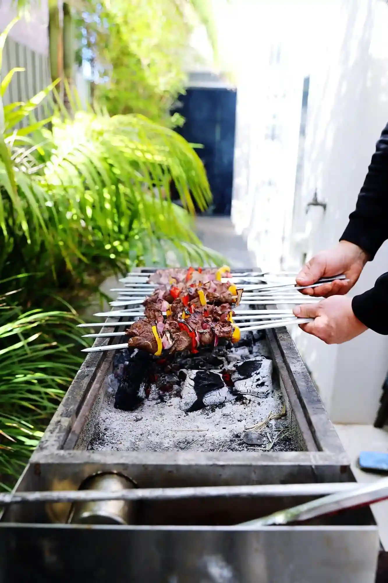 BBQ Event Catering Services in London chef grilling meat and vegetable skewers on charcoal barbecue in outdoor garden setting