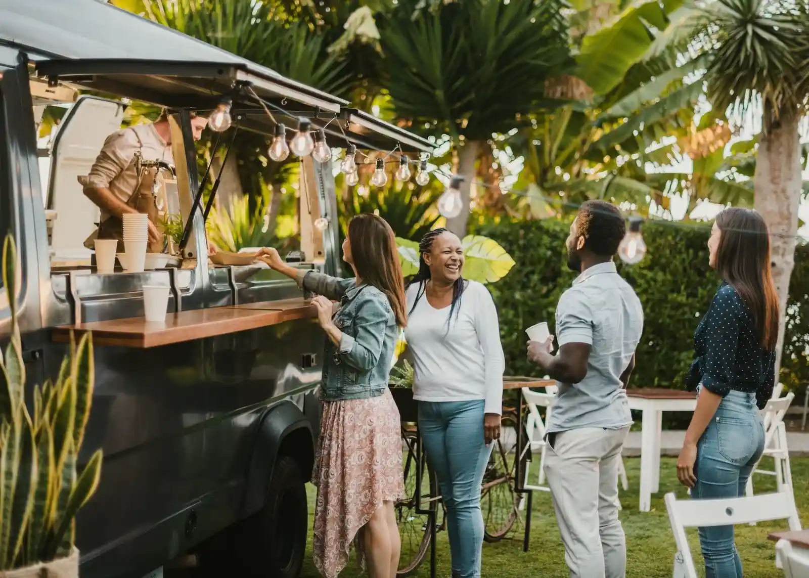 BBQ Event Catering Services in London with customers ordering from mobile food truck in tropical garden setting