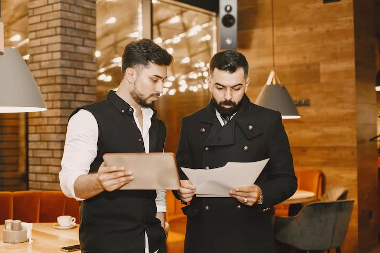 Two professional servers reviewing menu documents and tablet in upscale restaurant setting