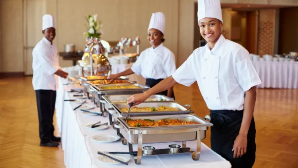 Buffet-style catering setup featuring a variety of hot and cold dishes arranged in serving trays on a decorated table.