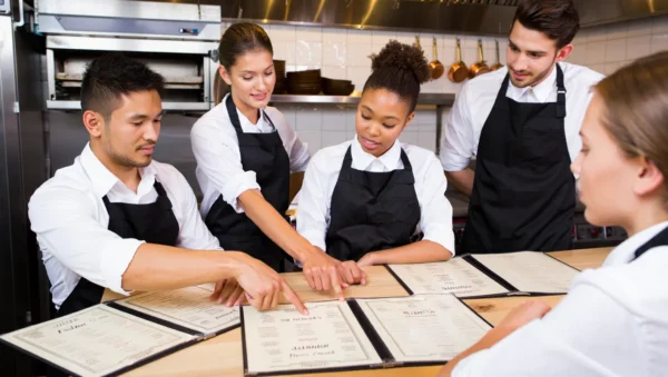Group of chefs collaborating in a kitchen while creating a custom Italian menu, surrounded by fresh ingredients and recipe notes.