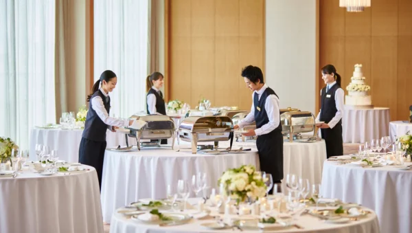 Catering team members arranging a beautifully decorated wedding dining setup with floral accents and elegant tableware for professional wedding catering.