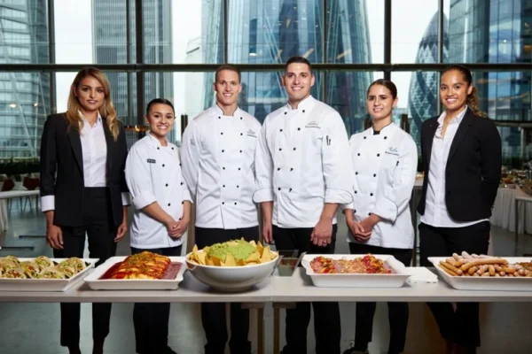 A professional Mexican catering team in London standing behind a table of authentic Mexican dishes, showcasing high-quality service for events.