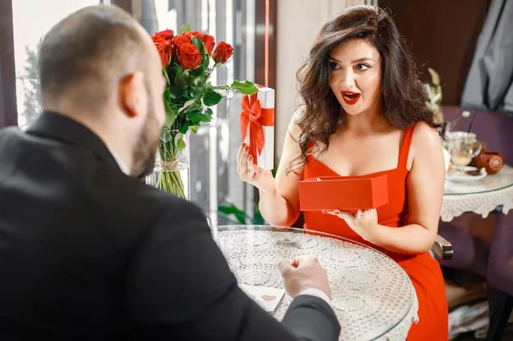 Woman receiving gift box with roses at cafe table