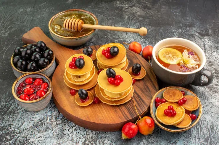 Pancakes with berries and honey on a wooden board