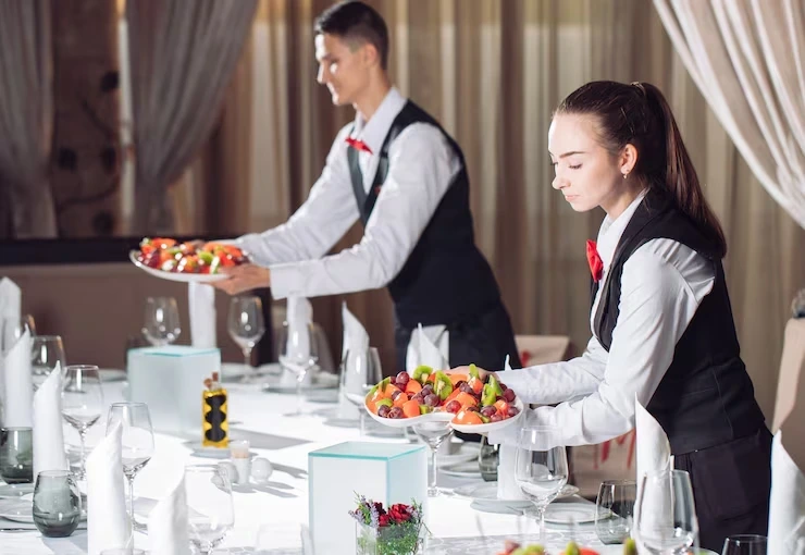 Two waitstaff serving fruit platters at formal table
