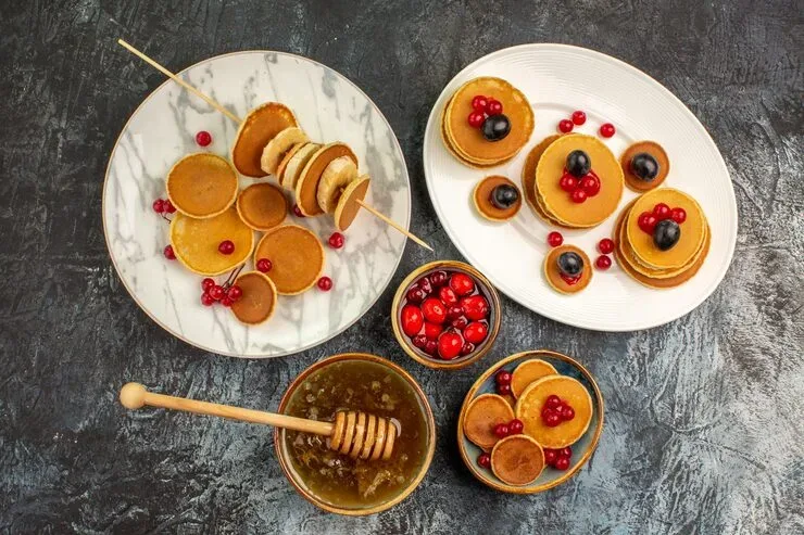 Pancakes with berries and honey on platters overhead