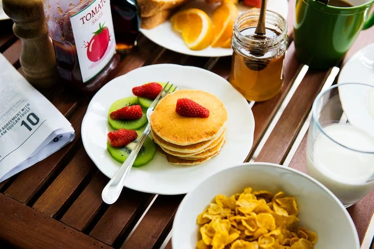 Stacked pancakes with strawberries and kiwi on table