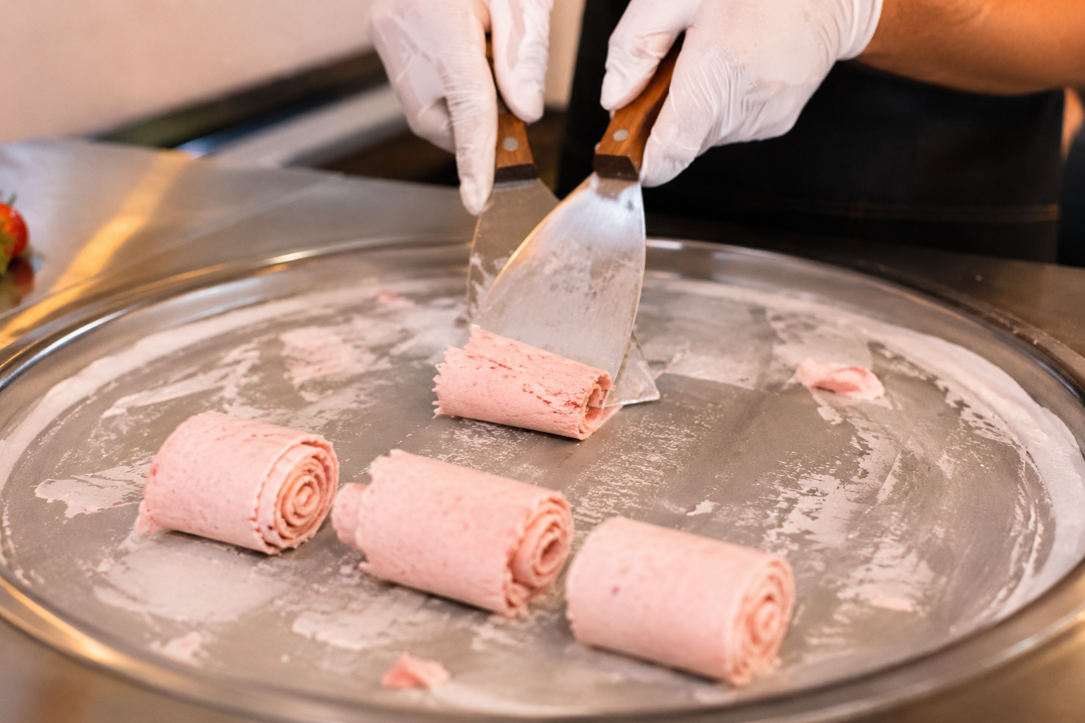 Fresh rolled ice cream being prepared on a frozen plate with metal spatulas, featuring hand-rolled ice cream rolls in a live catering station setup.