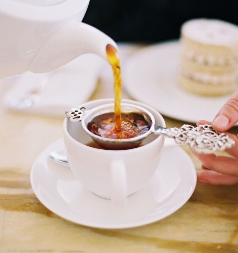 A person pouring a cup of tea, using a strainer. Elegant afternoon tea.