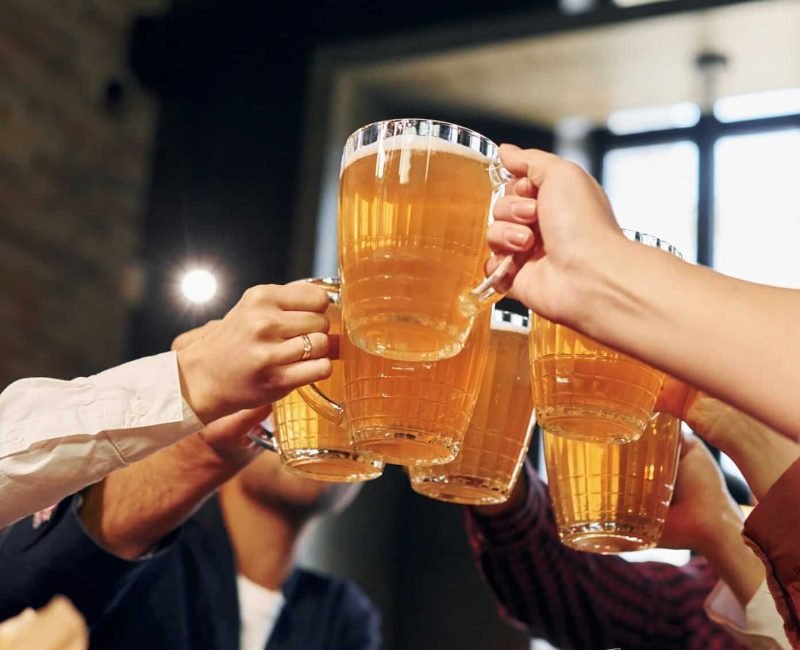 Cheering together. Group of young friends sitting in bar with beer