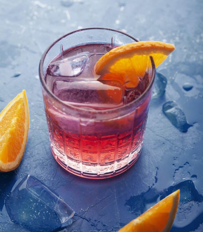Fresh ice tea summer cocktail with orange and ice. Background toned in modern blue color 2020