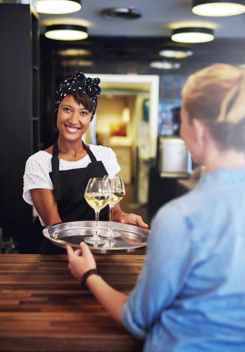 Smiling bartender serving glasses of white wine