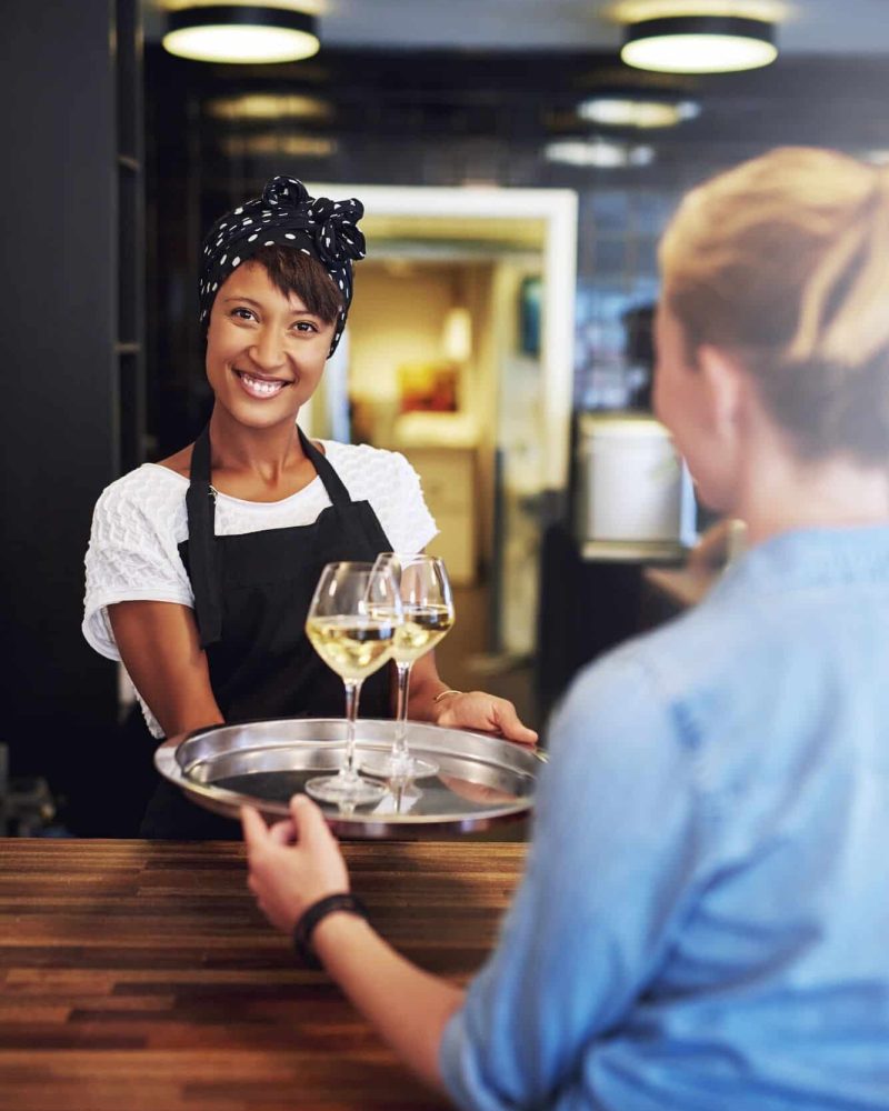 Smiling bartender serving glasses of white wine