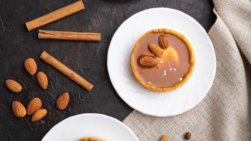 Sweet tartlets with almonds and caramel cream with cup of coffee on a black concrete background