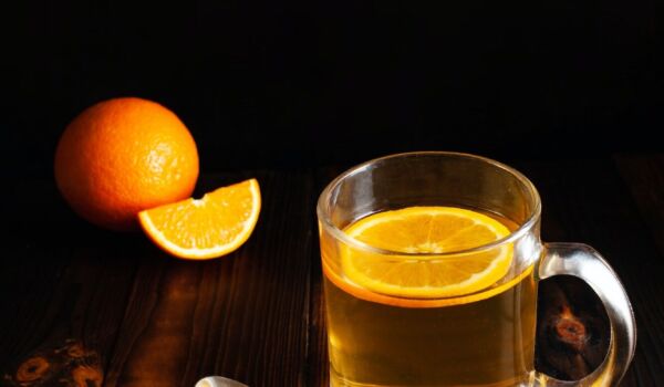 Tea with orange, sprinkled sugar, sliced orange, wooden brown backgroun