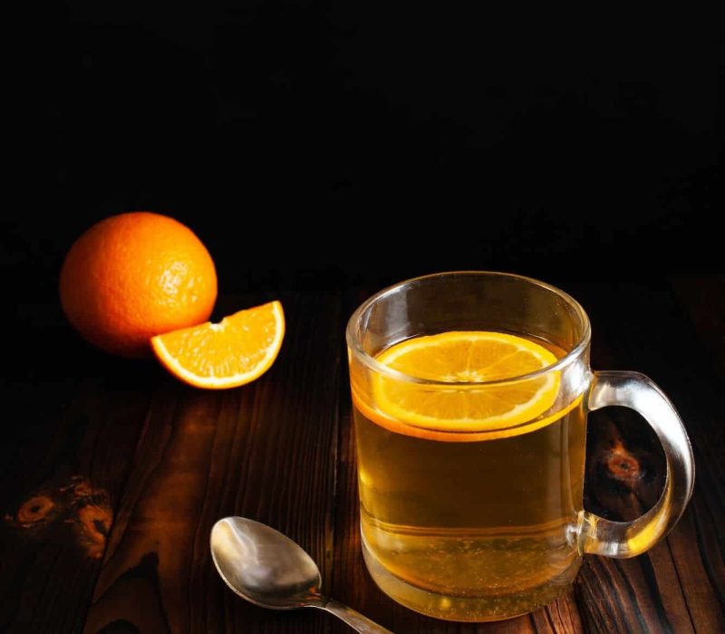 Tea with orange, sprinkled sugar, sliced orange, wooden brown backgroun